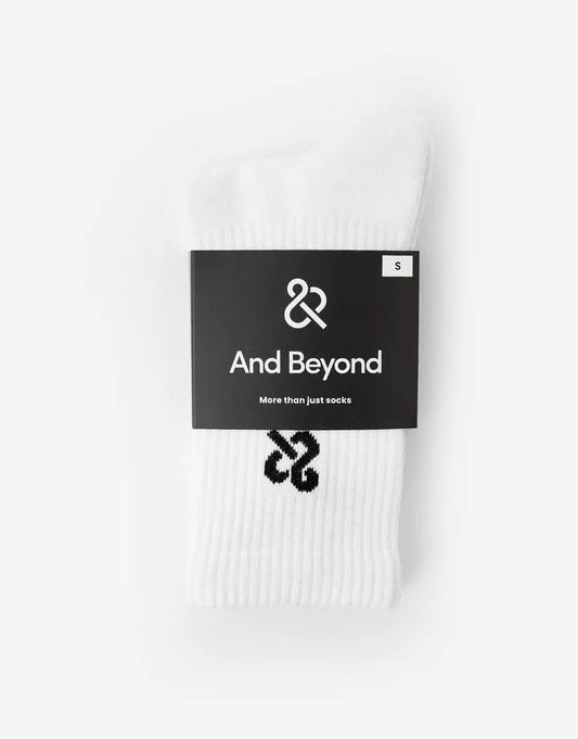 A pair of white And Beyond socks with a visible logo on the ankle area, packaged in a single sock packaging with a black label.