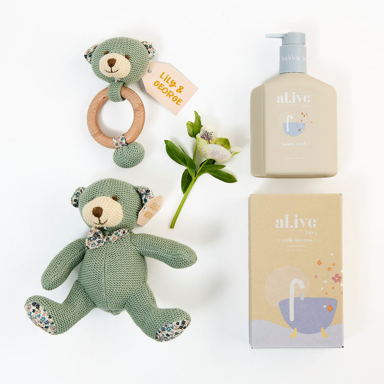 A set of baby bath and care products including a green knitted bear rattle, a beige bear teether, a baby bubble bath bottle, and a box of bath essentials from Al.ive.