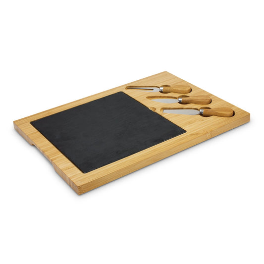 A wooden cheese board with a slate surface and three cheese knives with wooden handles positioned on top of the board.