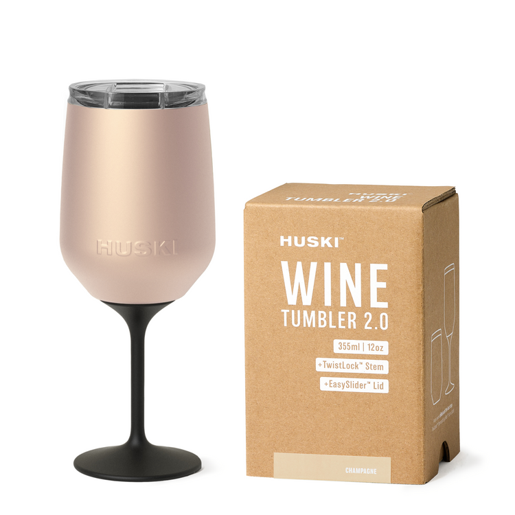 A golden Huski Wine Tumbler 2.0 with a clear glass top and black base, displayed next to its packaging box.