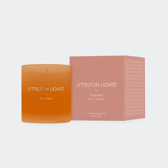 Orange candle with 'Lyttelton Lights' branding next to its packaging on a light gray background